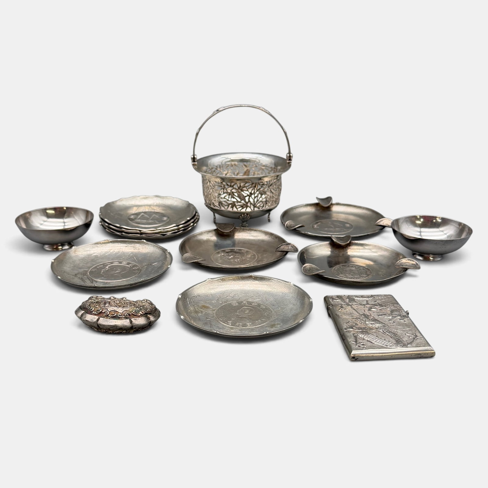 Group of Chinese Silver Ashtrays and Other Vessels: 9 ashtrays, each with silver Chinese coins to center. Two small sterling dishes, a sterling Cantonese calling card case, a sterling lock and a sterling Cantonese bowl. Total weight: 25.82 troy ounces
