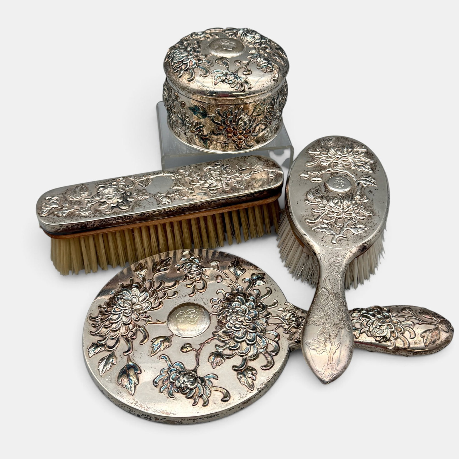 A Hung Chong Chinese Silver Dresser Set: Four pieces ladies dresser set in sterling silver, decorated with chrysanthemums. Sterling box weighs 9.13 troy ounces. Also includes a mirror and pair of brushes.