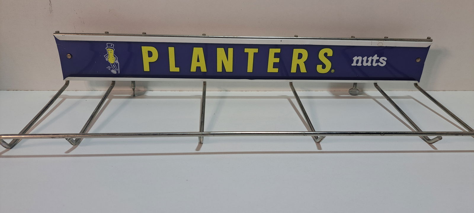 Planters Peanuts wire rack: wire shelf to hold bags of Planters Peanuts with tin sign, made to fasten on shelf, good condition, approx. 7" x 17.5" x 3", Please note: if picking up, location is different than auction location. Pl