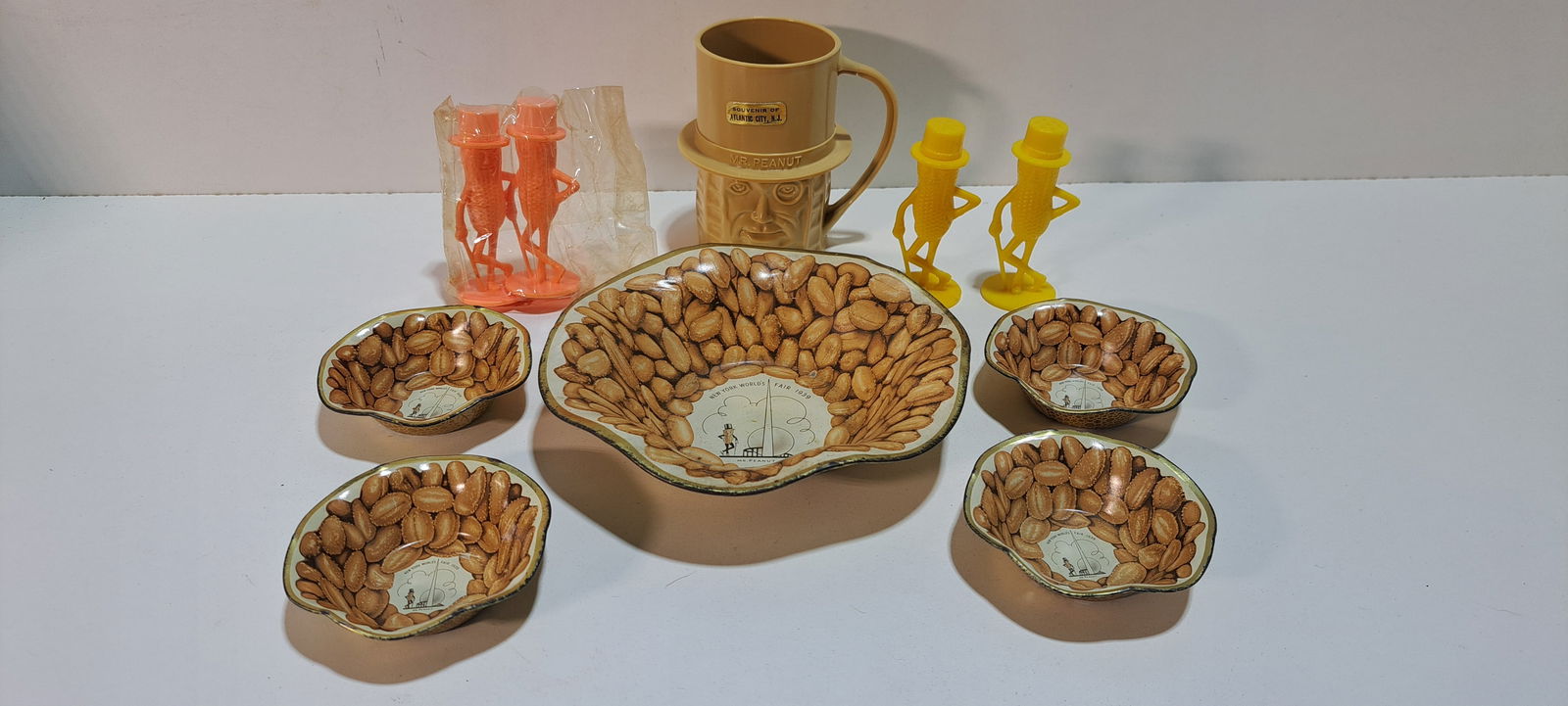 Planter Peanuts lot: Planters Peanuts collectible lot consisting of: tan plastic cup(has damage), pink salt and pepper shaker set still in plastic, yellow salt and pepper shaker set, set of 5 metal nut dishes from 1939