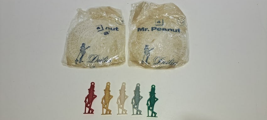 Mr. Peanut doilies and charms: lot consisting of: 2 packs of white, plastic, Mr. Peanut doilies, each containing 4 pieces, in original cellophane, also 5 plastic Mr. Peanut charms, red, tan, green, blue, white, each approx.