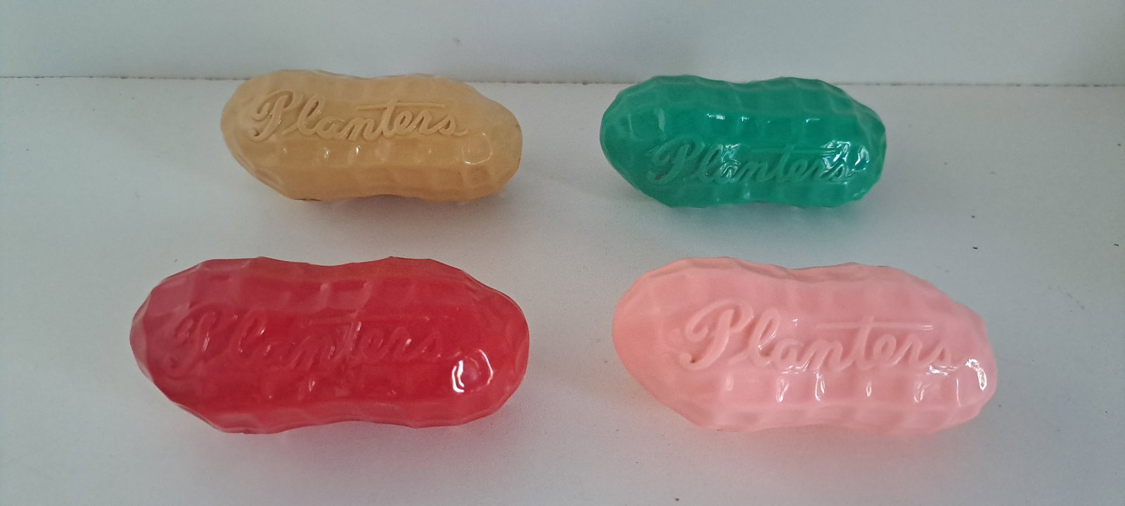 (4) 2-piece plastic peanut containers: Lot of 4, 2- piece, plastic, peanut shaped containers. Embossed "Planters" in script lettering. Tan, green, pink, and red. Good condition. Each approx. 4" long. Please see our shipping policy for
