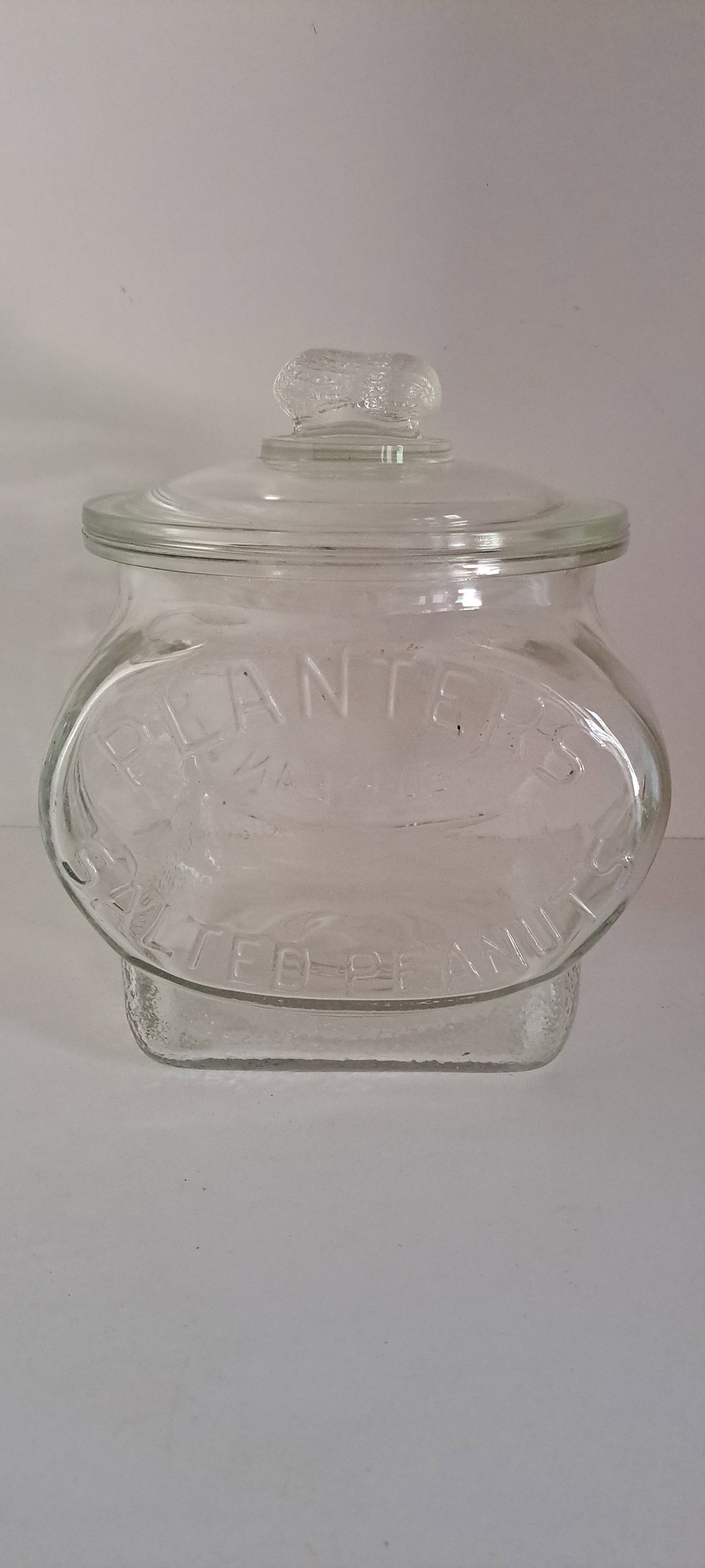Planters Peanuts football jar: Planters Peanuts, glass counter jar, shaped like a football. Has original lid with peanut shaped handle. Made in USA on bottom. This is an original jar, not a reproduction. Rim of jar has some minor