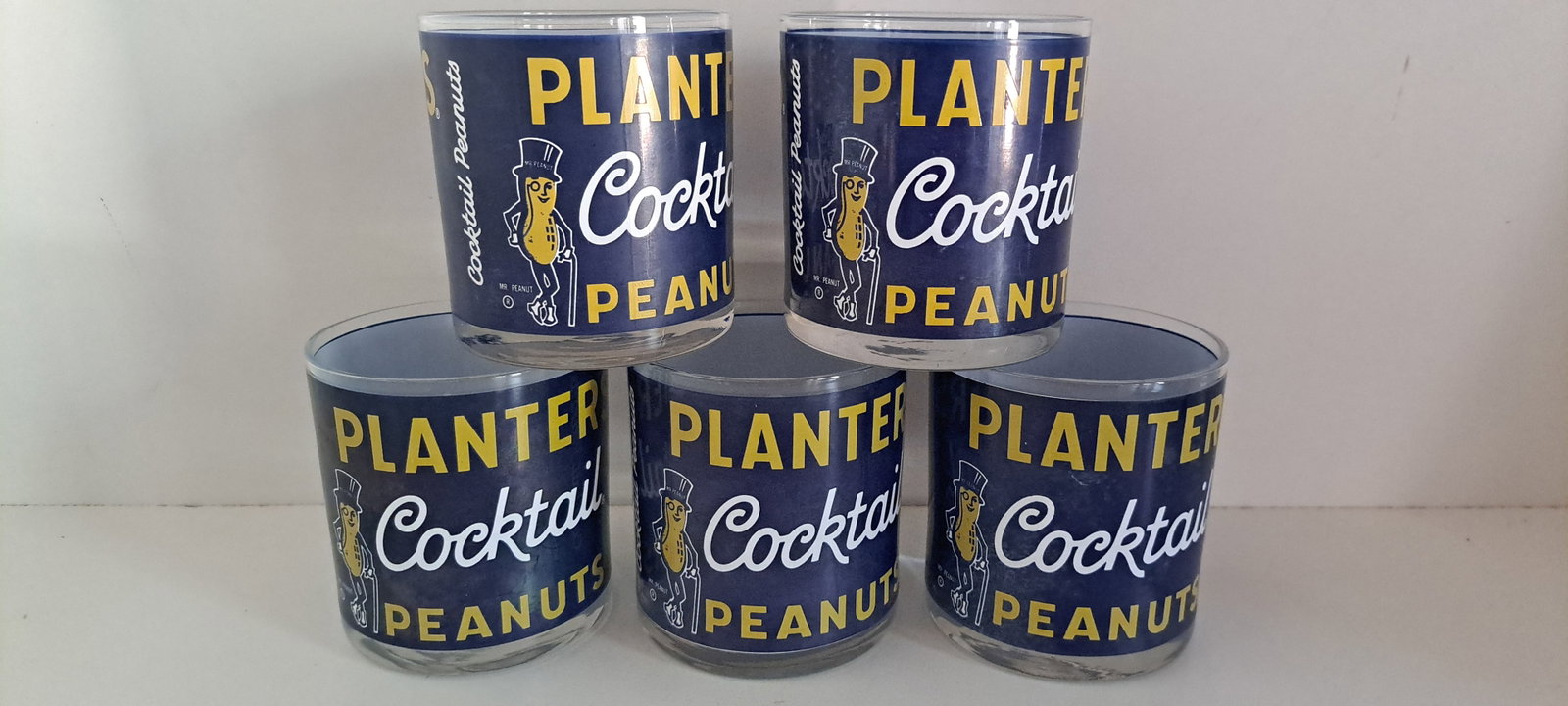 (5) Planters Peanut glasses: Set of 5 short glasses, made to look like cans of Planters cocktail peanuts, with Mr. Peanut. Show minor storage wear, no chips or cracks. Each approx. 3.5" tall. Please see our shipping policy for