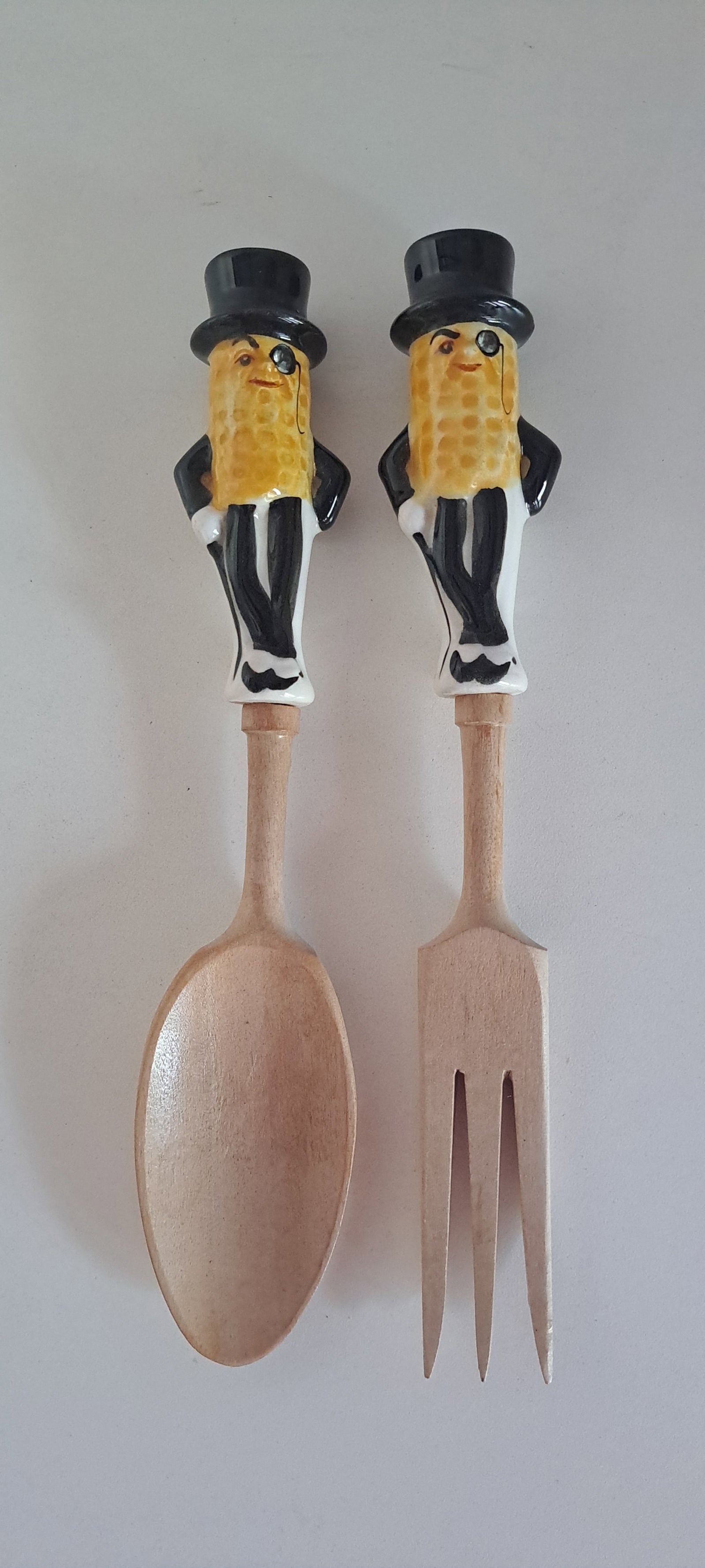 Mr. Peanut ceramic salad fork & spoon: Wooden salad fork & spoon with ceramic, figural, Mr. Peanut handles. Both have a rhinestone in his monocle. Original stickers. Minor chip on back of spoon. Approx. 10" long. Please see our shipping