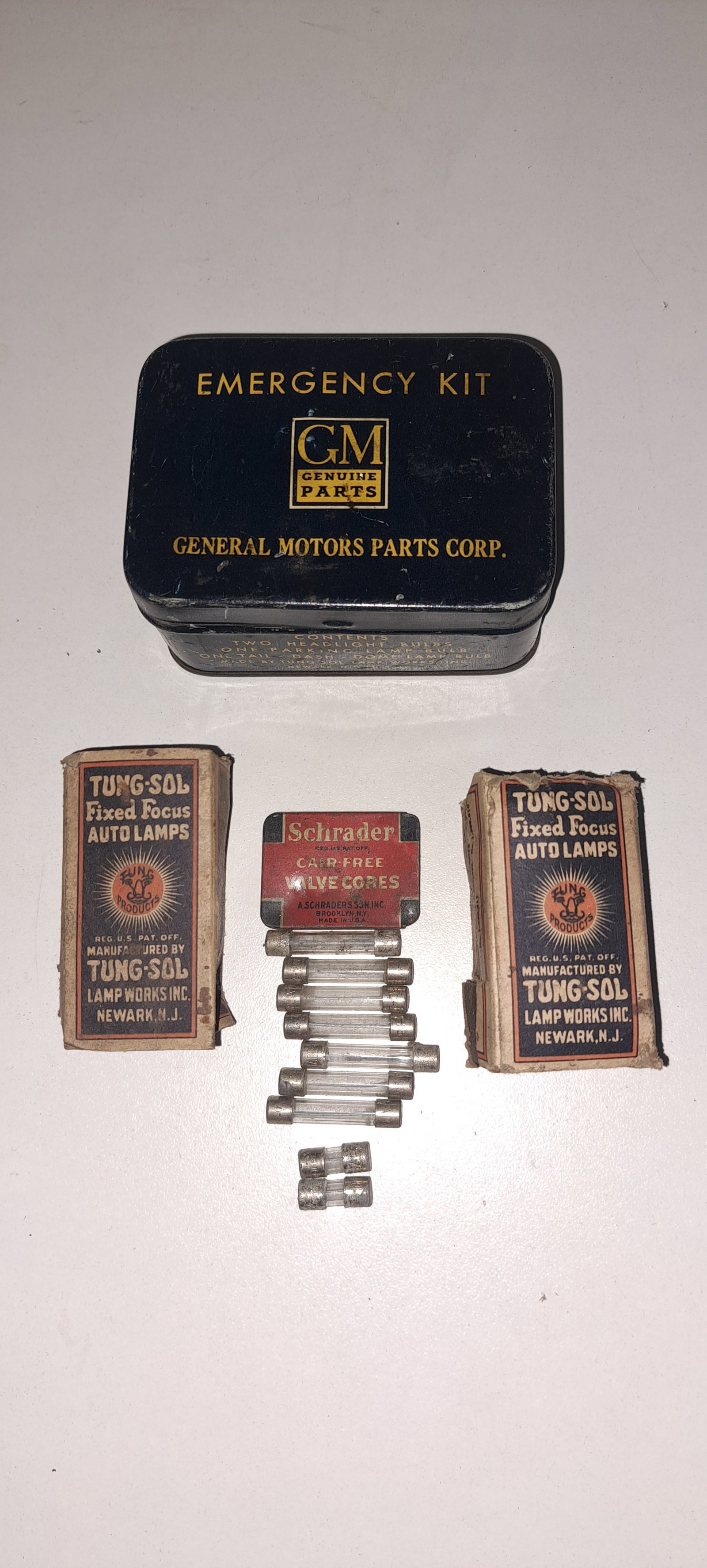 GM emergency kit: Early, tin, General Motors, Emergency Kit. Includes (2) Tung-Sol light bulbs in cardboard sleeves, various fuses, and Schrader valve cores. Approx. 2.5" x 3.75" x 1.5" . Minor wear, overall good