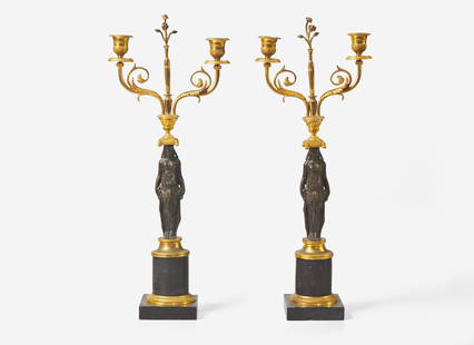 A pair of French Empire gilt and patinated bronze candelabras, first quarter 19th century Of: A pair of French Empire gilt and patinated bronze candelabras, first quarter 19th century Of Neoclassical form, with caryatids supporting scrolled candle cups, on black marble bases. H: 20 ¼ in.
