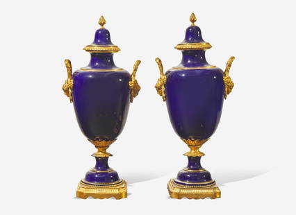 A pair of French gilt bronze mounted cobalt blue porcelain urns, late 19th / early 20th century: A pair of French gilt bronze mounted cobalt blue porcelain urns, late 19th / early 20th century The vase with gilt borders, with handles in the form of masques, the covers with finials, apparently unm