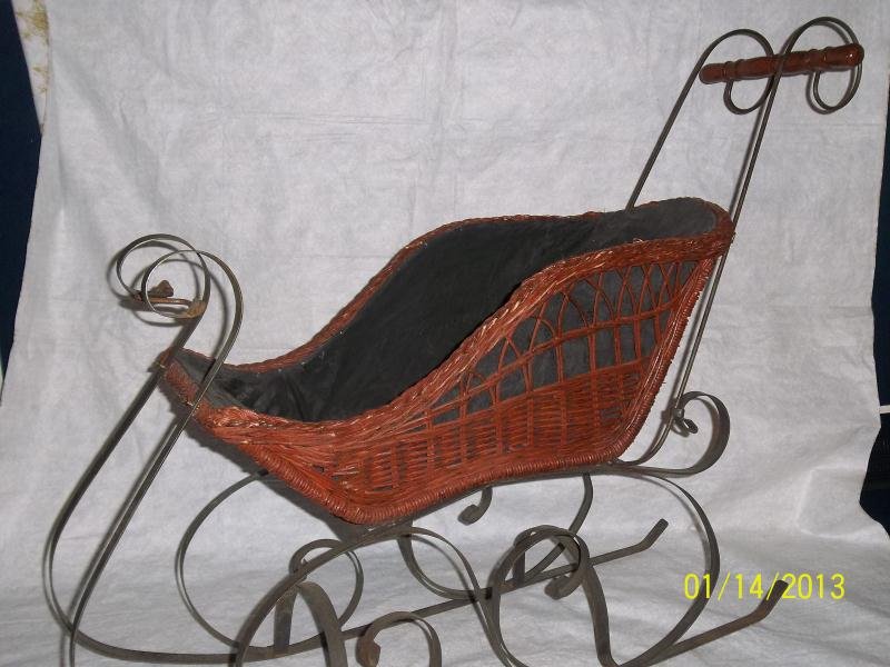 Doll's wicker mini sleigh with curved metal metal: Doll's wicker mini sleigh with curved metal metal runners, black wooden handle, black interior cloth lining, sleigh black wooden handle, 15-75, black interior cloth lining, sleigh measures 21" h x 26"