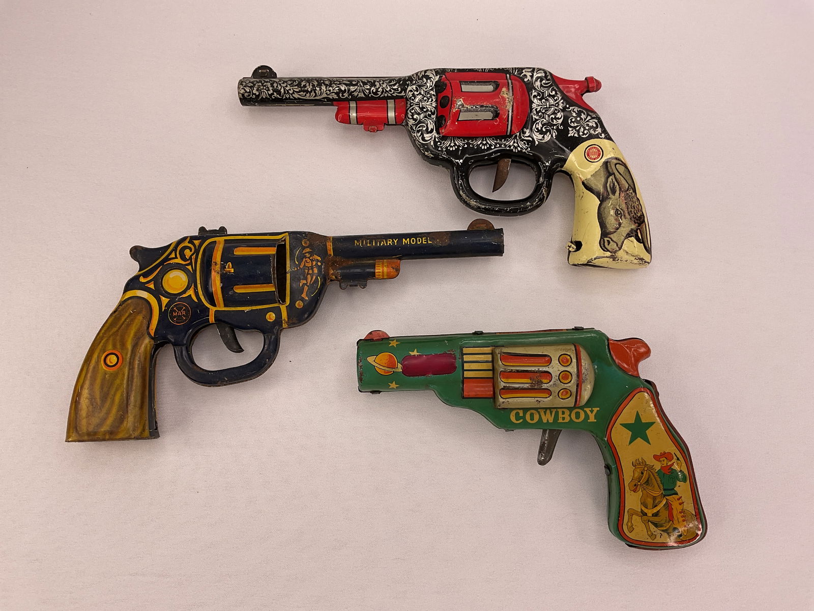 (3) Vintage Tin Clicker 6 Shooter Guns OHIO Art - MARX Cowboy Spark Japan Gun: (2) Vintage Tin Clicker 6 Shooter Guns - Bull on Handle made by OHIO Art clicks when trigger is pulled. Military Model .45 made by MARX clicks when trigger is pulled. Gun marked COWBOY on side Made in