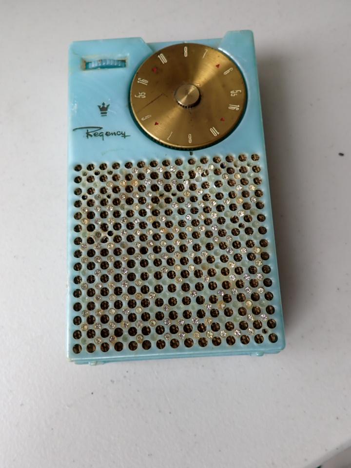 Regency TR-1. 1956 Jeweled Iridescent with Rhinestones Radio: Sky Blue. Untested. Missing some rhinestones. Small spot on front grill by speaker is indented with small break in plastic. Has some edge chipping. Some tape marks on reverse and minor scuffing on fro