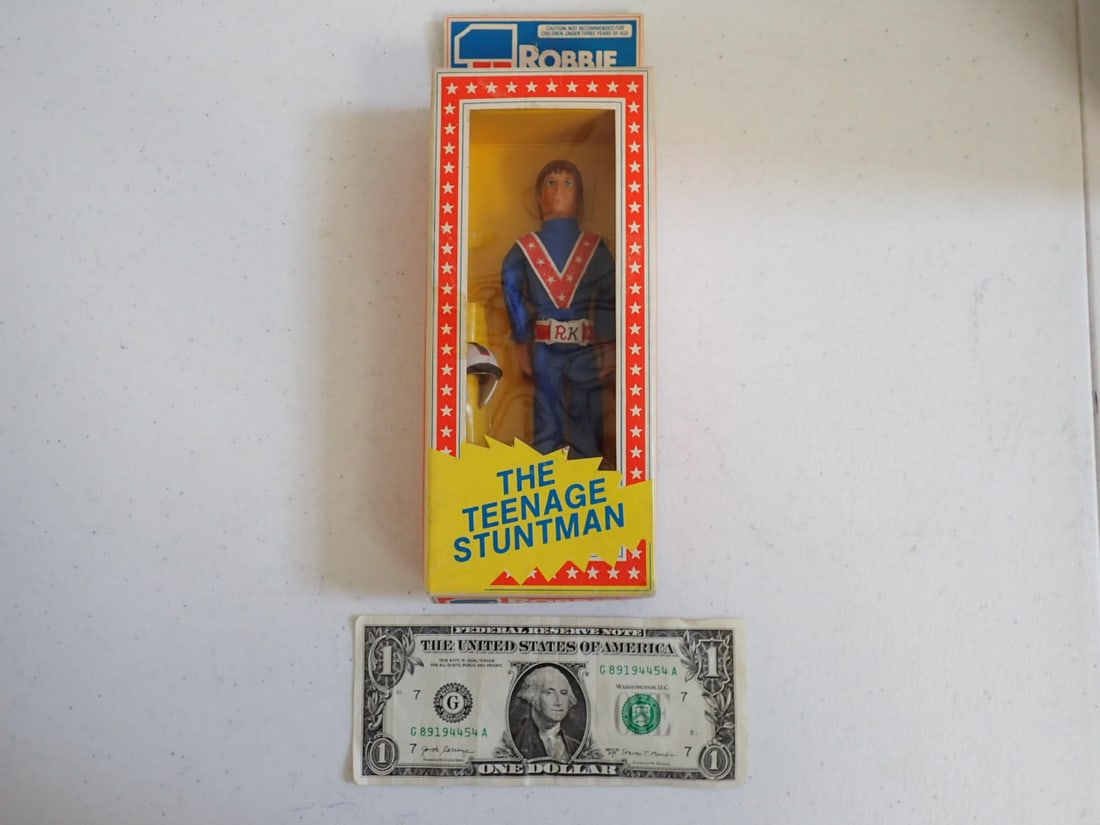 1976 Ideal Robbie Knievel "The Teenage Stunt Man" Figure: Flexible Action Figure with Helmet. Unopened in package. Unpunched. Original Tap on Top. No Tape on Bottom. Some wear on box. Some scuffing on box and minor marks on cellophane Panel. Small tear on re