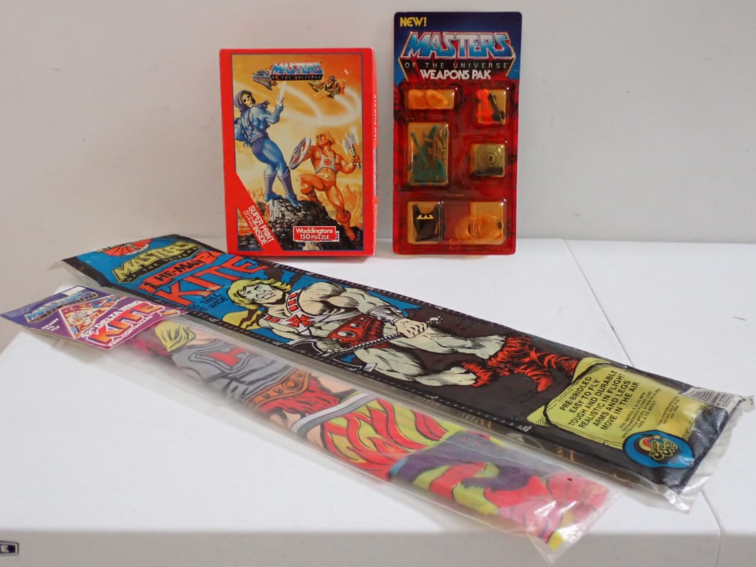 1980's Master of the Universe Kites, Weapons Pak & Puzzle: He-Man Kite in package has some wear. Kite is 55" x 25" and Delta Wing Kite is 42" Keel Controlled. Weapons Pak is MOC - Unpunched Punch Insert is loose. Some staining and creasing. Puzzle in opened b