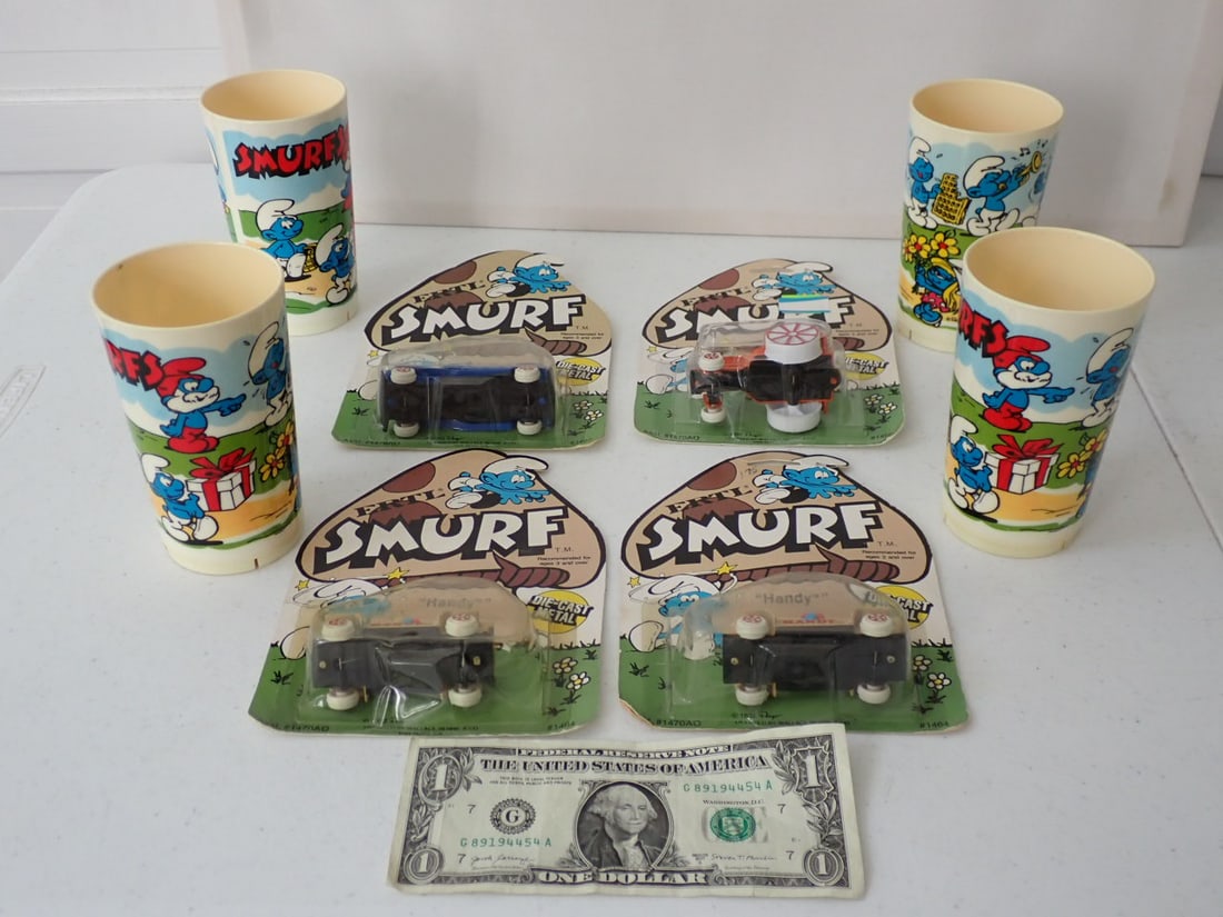 4 1982 Smurf Ertle Diecast Cars, Tumblers with Original Stickers: Ertle Cars Sealed in Original Packages and 4 11 ounce tumblers 2 with original stickers. Packages have a little wear and staining. Tumblers have some discoloration.