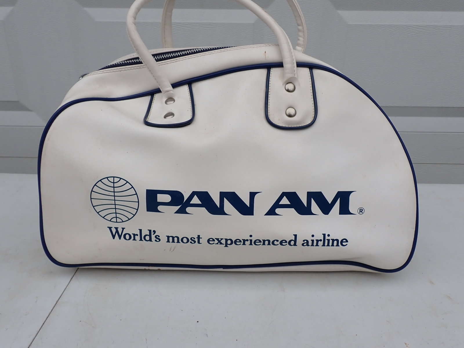 White with Blue Lettering Pan Am Travel Bag: "Pan Am World's Most Experienced Airline". Vinyl Canvas Lined. 18" wide x 12" high Excluding handles. A little soiling.