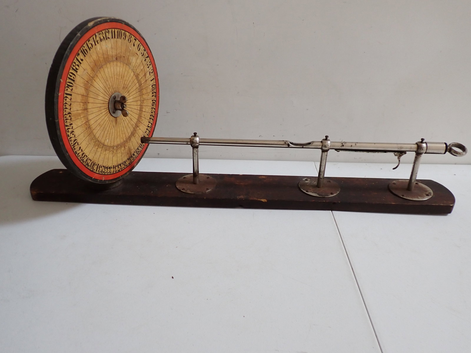 Gaming Wheel on Board with Nickel plate Bar & Trigger: 48 numbers gaming wheel. Wheel is 13" diameter. Nickel plate bar with trigger is 28". Board is 39". Board has wear with discoloration on wheel and some rust on chrome.