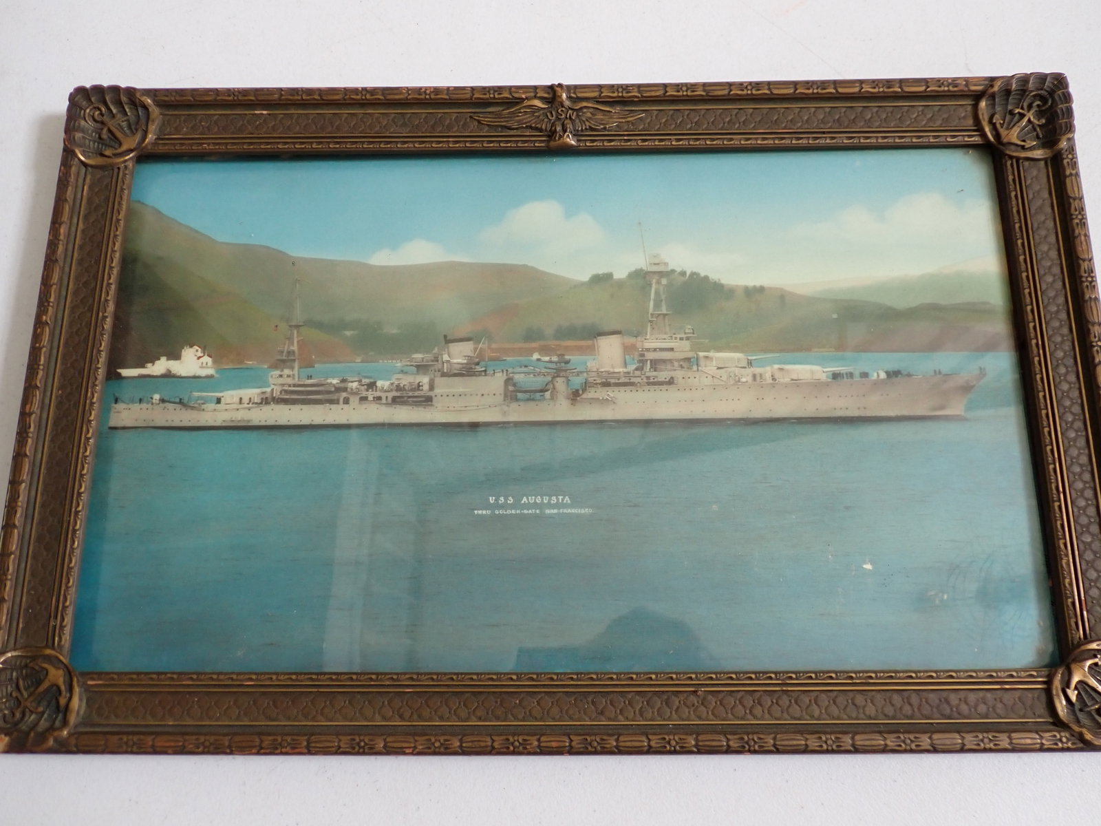 U.S.S. Augusta Hand Tinted Print in United States Navy Frame: Below ship it says U.S.S. Augusta Thru Golden-Gate San Francisco. Circa 1920s frame with USN and Eagle at Top and Anchors at Corners. Has some chipping of frame corner. Has some minor imperfections on