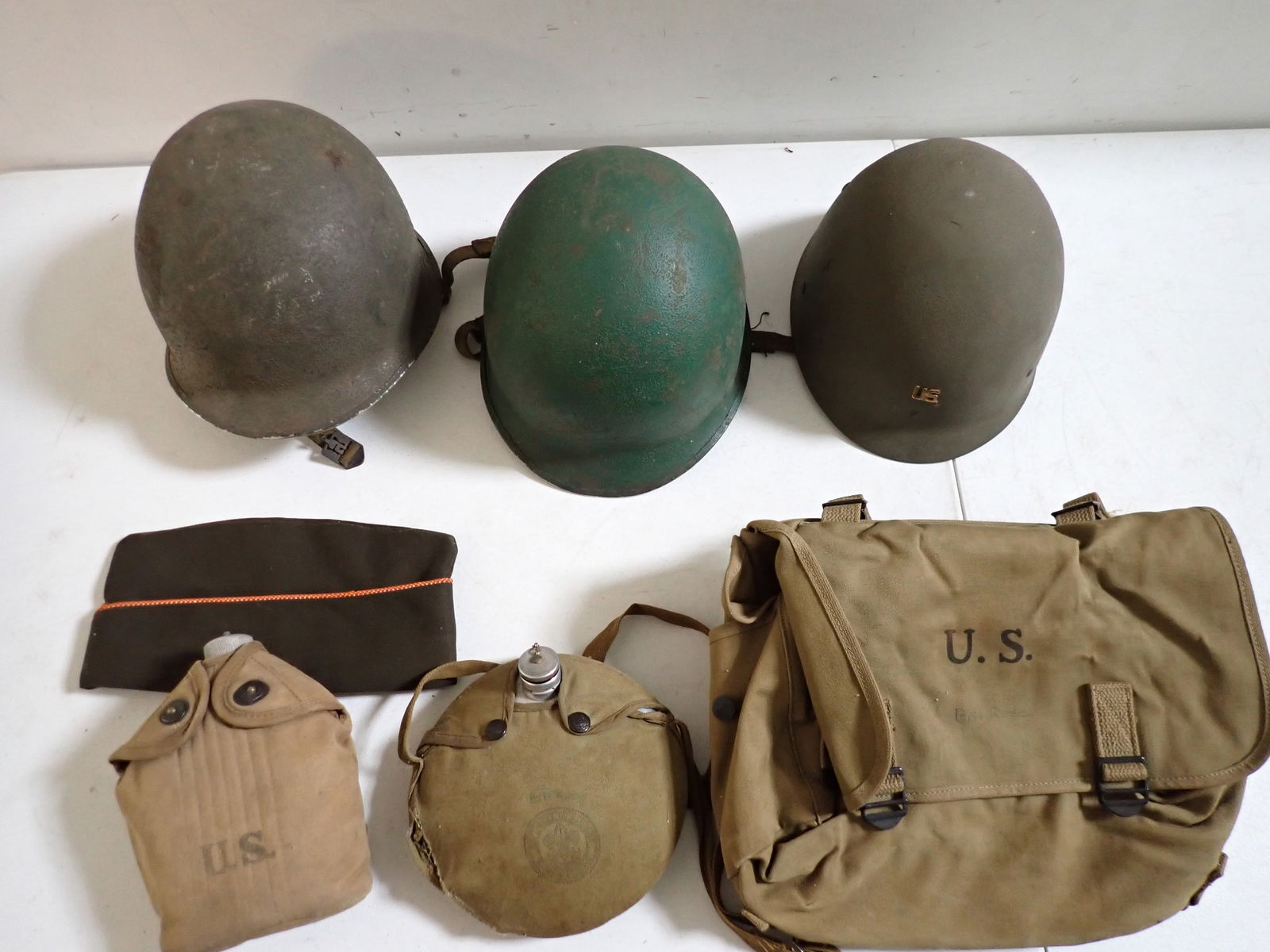 Military Helmets, Liners, Musette Bag, Canteens, and Garrison Cap: Helmets and Liners. One Military and One Boy Scout (torn cover) Canteens. Musette Field Bag. Garrison Cap. Show Normal wear.
