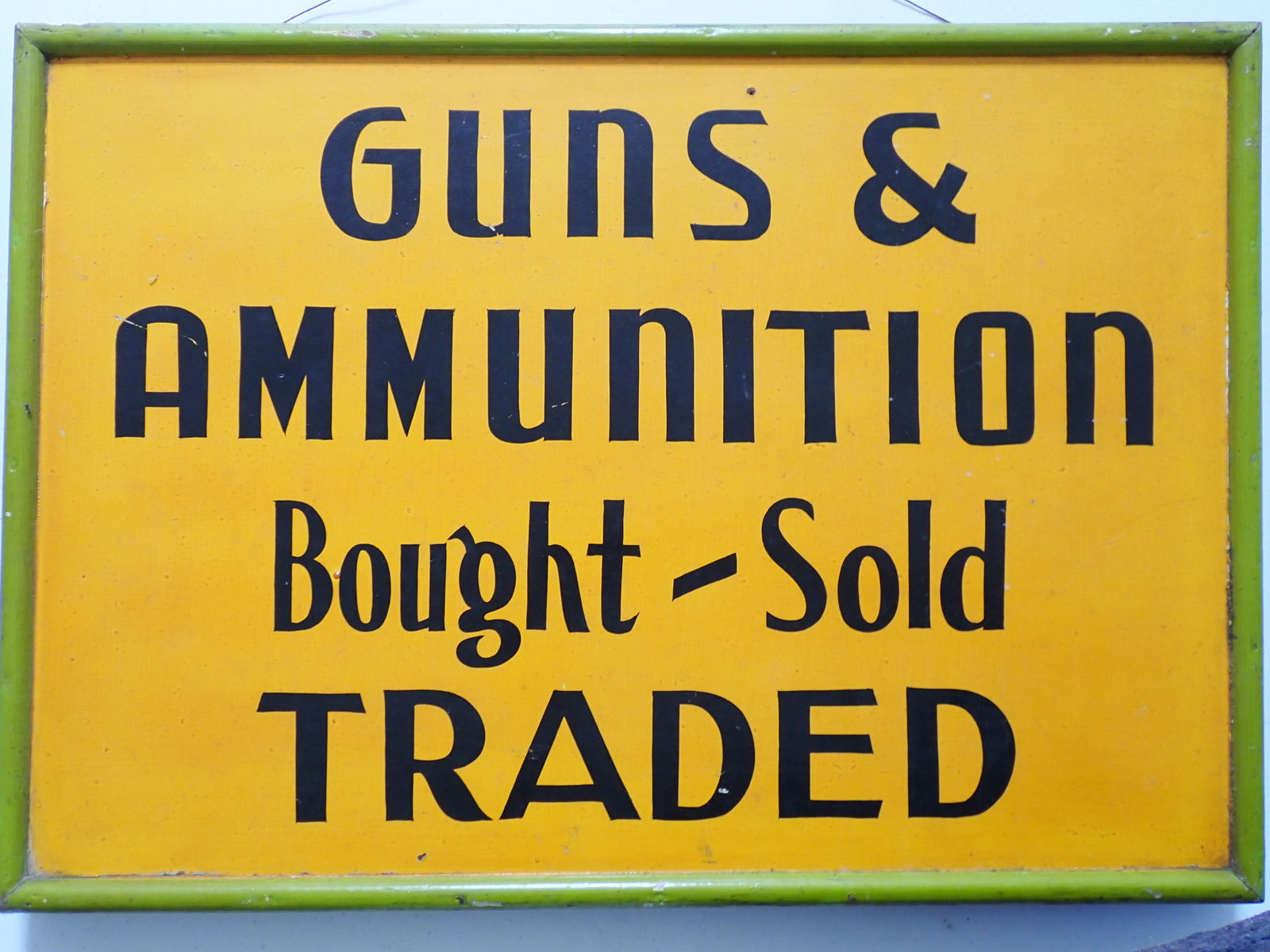 Guns & Ammunition Bought-Sold Traded-- Advertising sign: Vintage sign masonite and thick wood frame. Black letters on orange background with lime green border. 17" x 24". Good condition with a little wear.