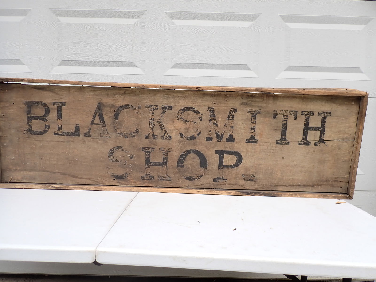 Primitive Antique Folk Art Wooden Blacksmith Sign: Wooden sign Wood Framed. 19" x 63". Shows some natural wear of lettering. Frame has some wood loss at corners. Some splitting of wood.