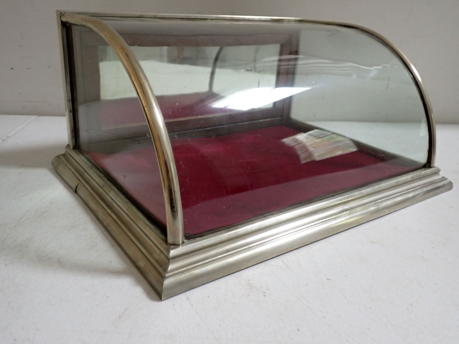 Small Country Store Steel Frame Curved Glass Countertop Display Case: Case has Metal Frame with Wood Back and Felt Lining. 13 1/2” Wide. 6 ½” High. 10” Deep. Curved Glass and Felt Lining. Has key. Mirrored back. Has crack to metal on base on one