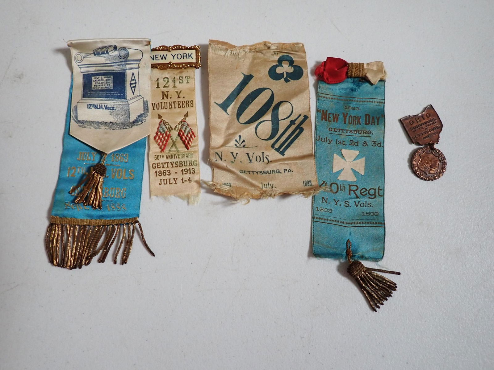Gettysburg reunion ribbons and medal: 3 New York regiments, New Hampshire, and Ohio Medal. One worn. One has large tear as can be seen in photo.
