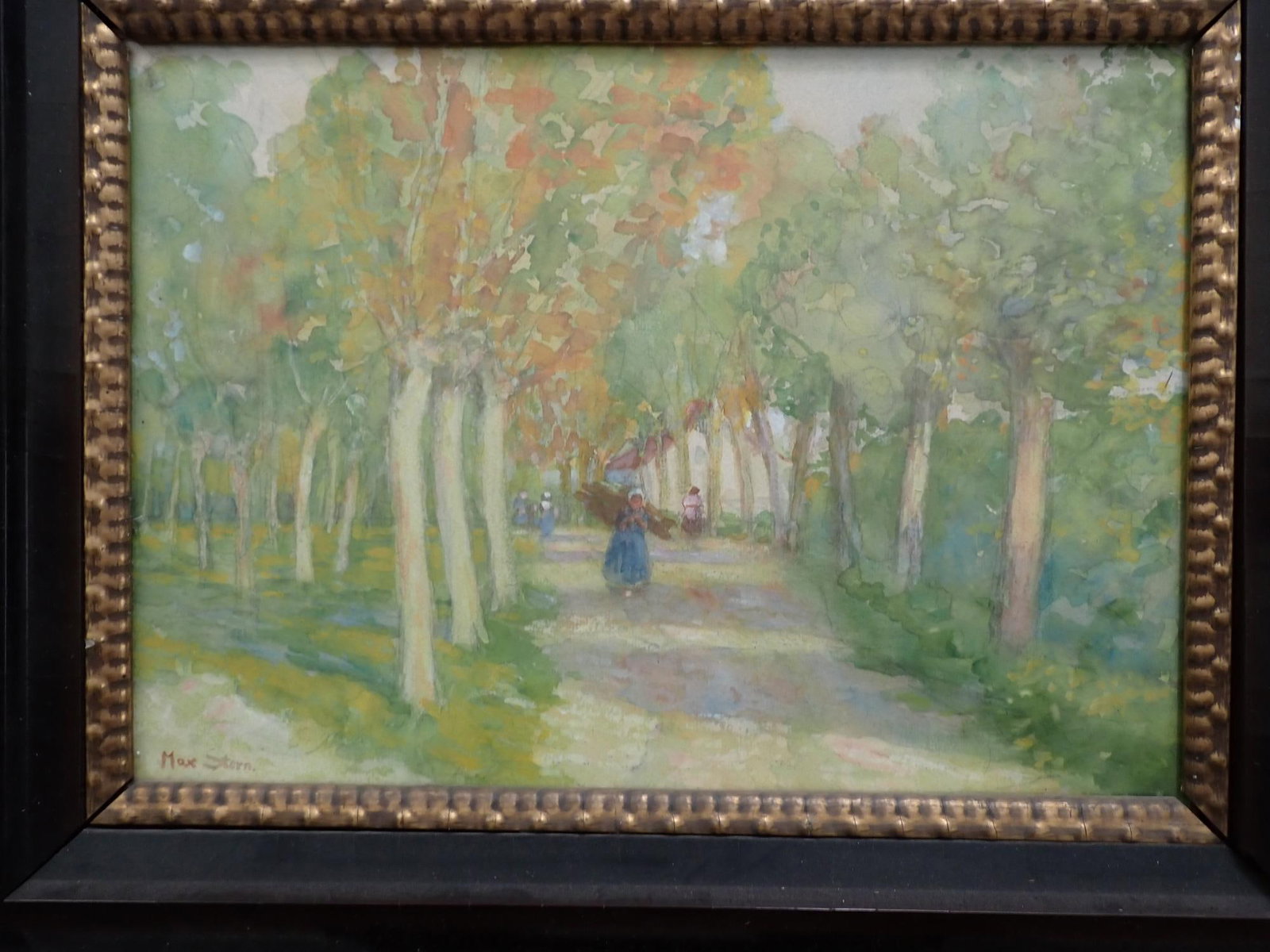 Max Stern Watercolor Country Road Painting: Shows woman carrying a bundle of sticks and others walking on a dirt road with colorful trees overhanging the road. Art approximately 12? x 16.? Frame 20? x 25.? Frame is loose at corner and has chipp