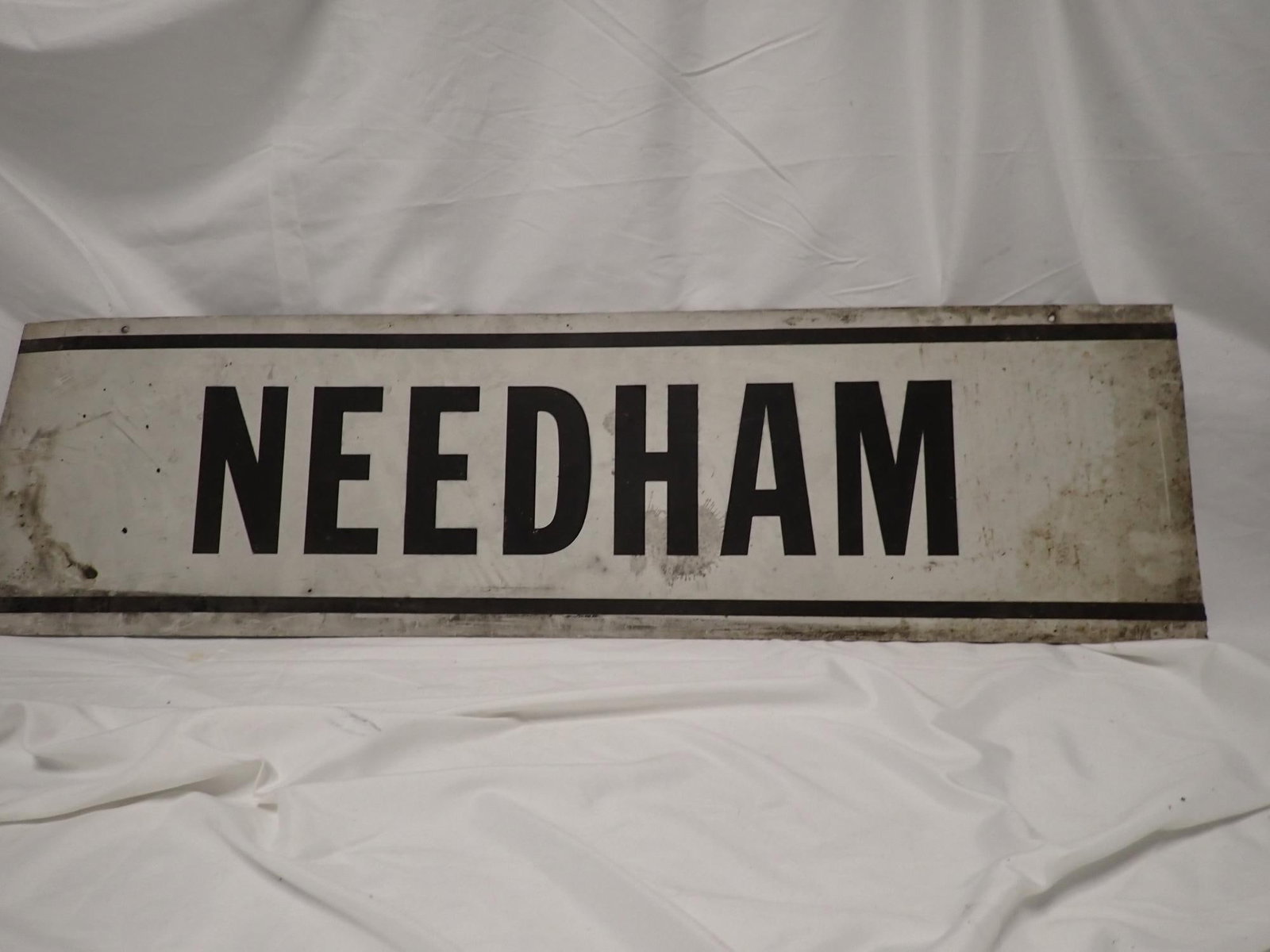 Needham Metal Railroad Sign: Sheet Metal Needham Sign. Has grease and staining from normal wear and some denting on left side. 10 1/4" x 36".