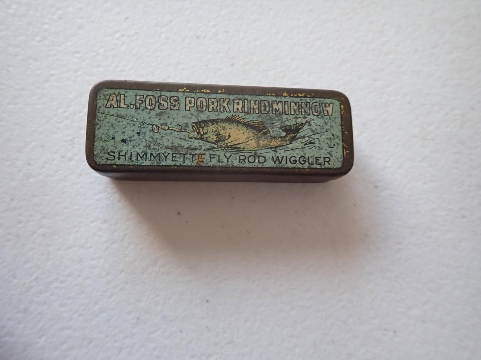 Al Foss Porkrind Minnow Fish Lure Tin: "Shimmyette Fly, Rod Wiggler." 2 5/8" x 7/8" Wear as seen in photos.