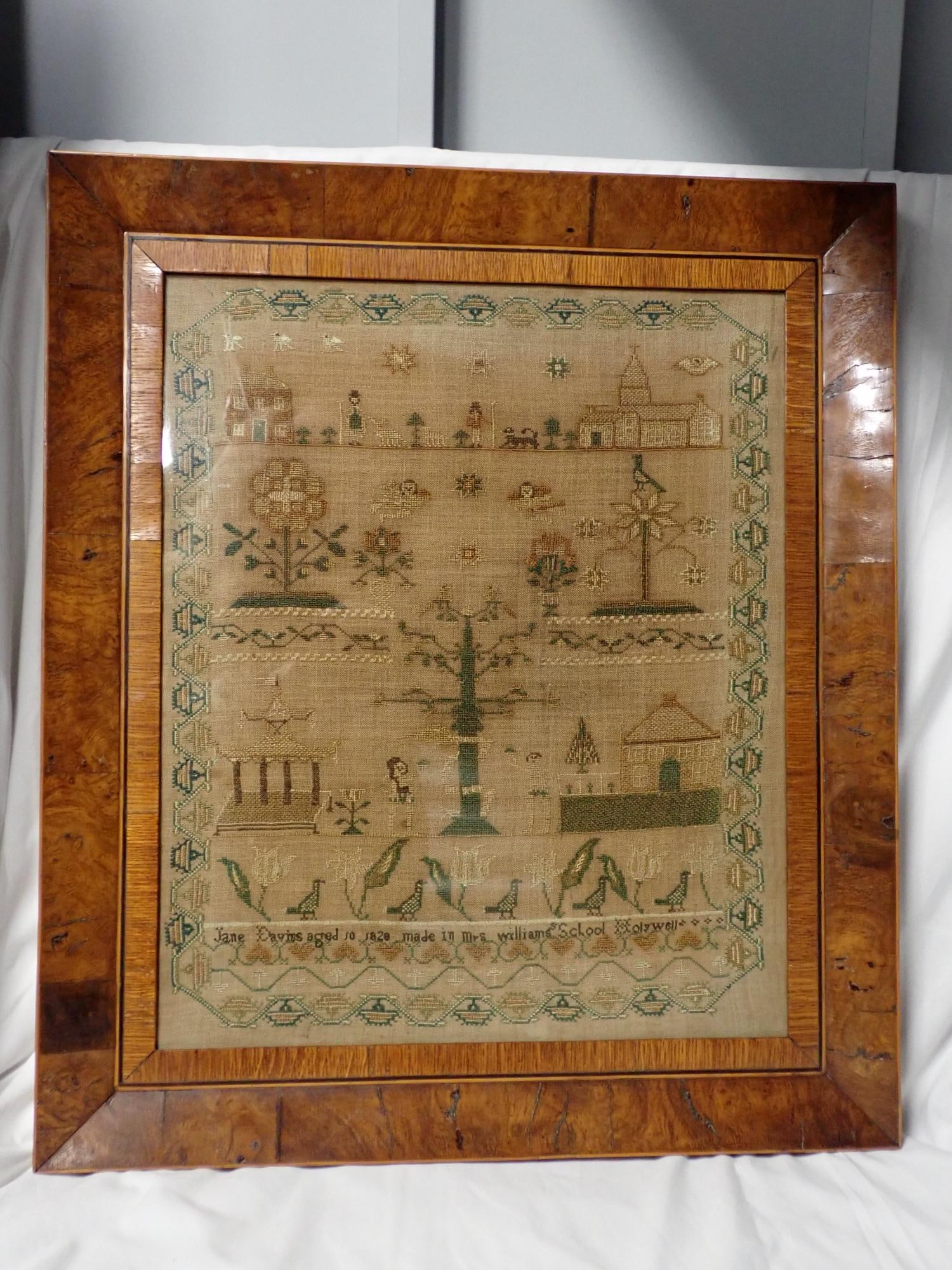 1820 Jane Davies (?) sampler: Jane Davies aged 10 1820 made in Mrs. Williams School Holywall (?) depicting buildings, people, animals and buildings of worship Frame 23 1/2" x 20 1/4" Sampler 18 1/2" x 15"