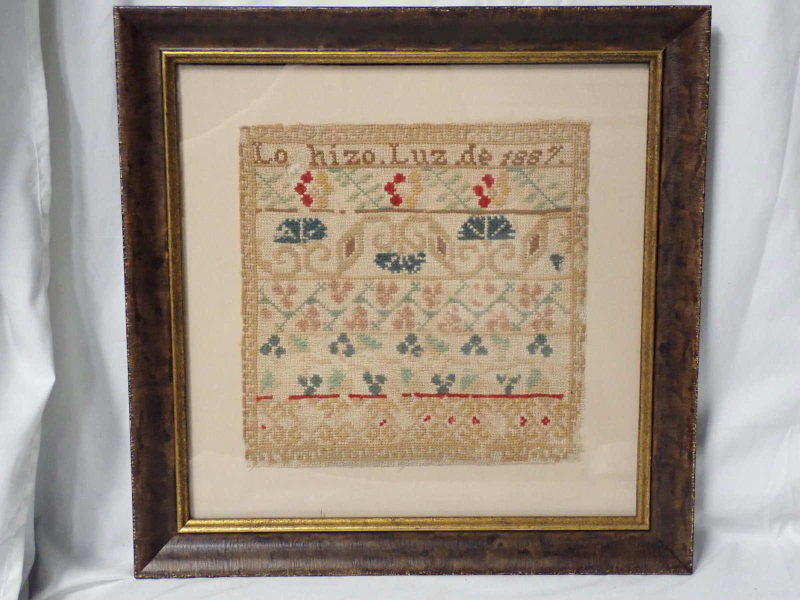 1887 Lo hizo. Luz Sampler: Lo hizo Luz de 1887 Motif of berries and vines with a geometric border. Some fabric and thread loss. Some fading. Frame 16" x 16" Sampler 9 1/2" x 9 1/2"