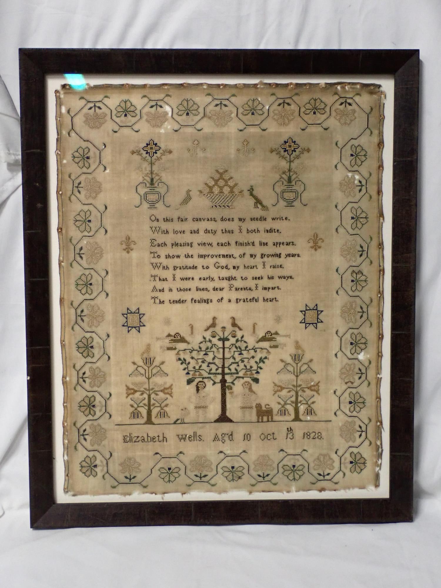 1828 Elizabeth Wells Sampler: Elizabeth Wells, Ag'd 10 Oct 13th 1828. Verse in center, Motif is Adam and Eve under tree, cherubs and birds and animals. Floral geometrical vince border design. Fabric loss and discoloration. Frame