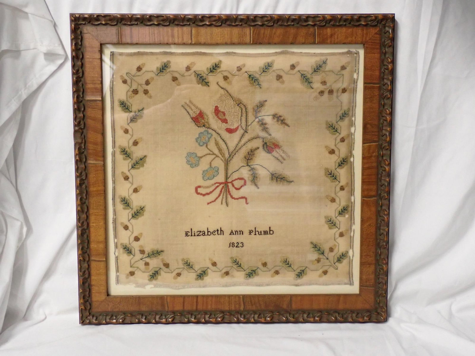 1823 Elizabeth Plumb Sampler: Elizabeth Ann Plumb 1823 Floral center with red bow. Border of acorns and leaves. Some discoloration and fabric loss. Frame 16 3/4" x 17" Sampler 12 3/4" x 13 1/4 ."