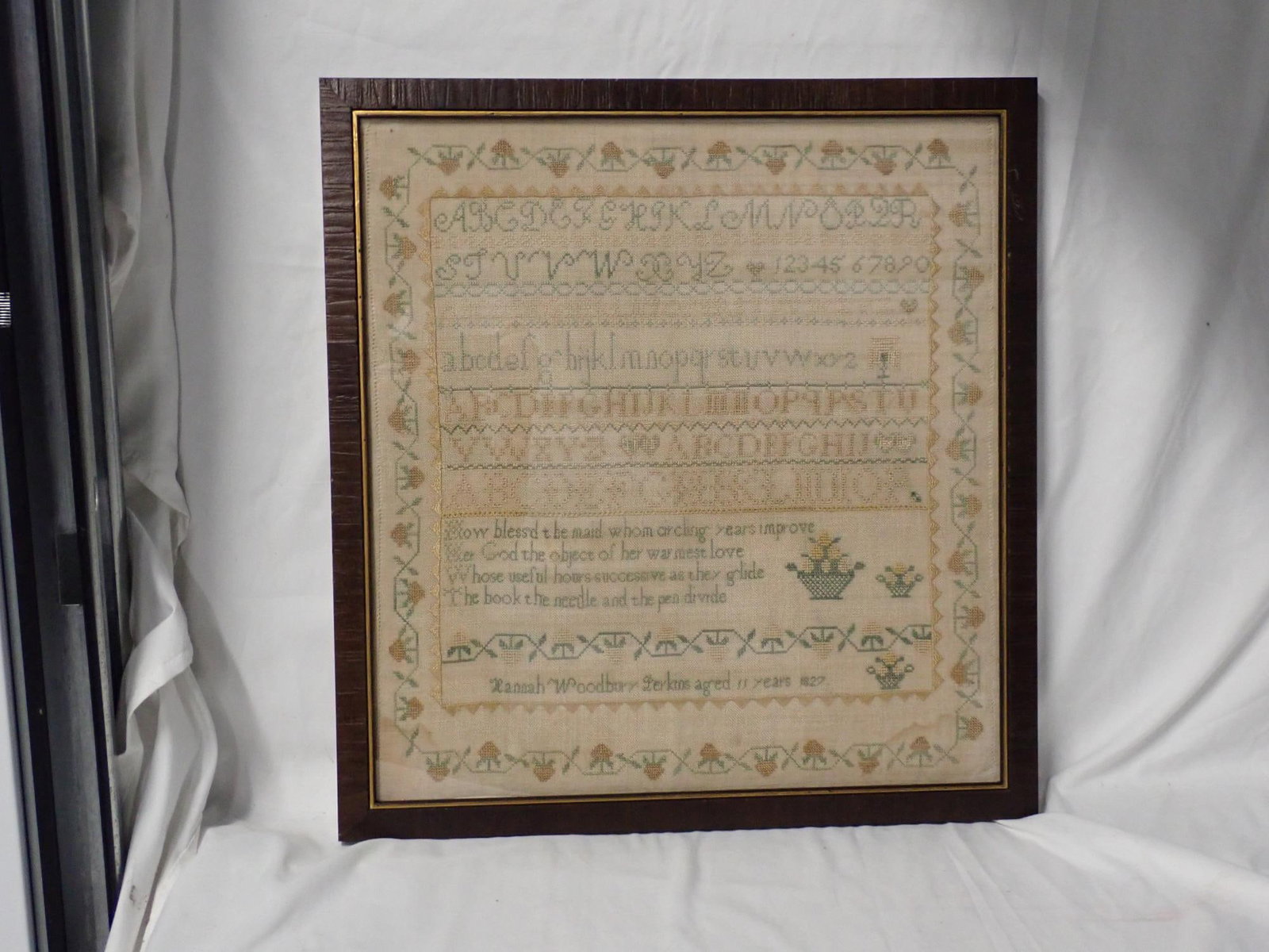 1827 Hannah Woodbury Perkins Sampler: Hannah Woodbury Perkins aged 11 years 1827. Alphabet and numbers, some stitching is eyelet stitch. Border of vines and flowers. Religious verse at bottom. Some slight staining in right bottom corner