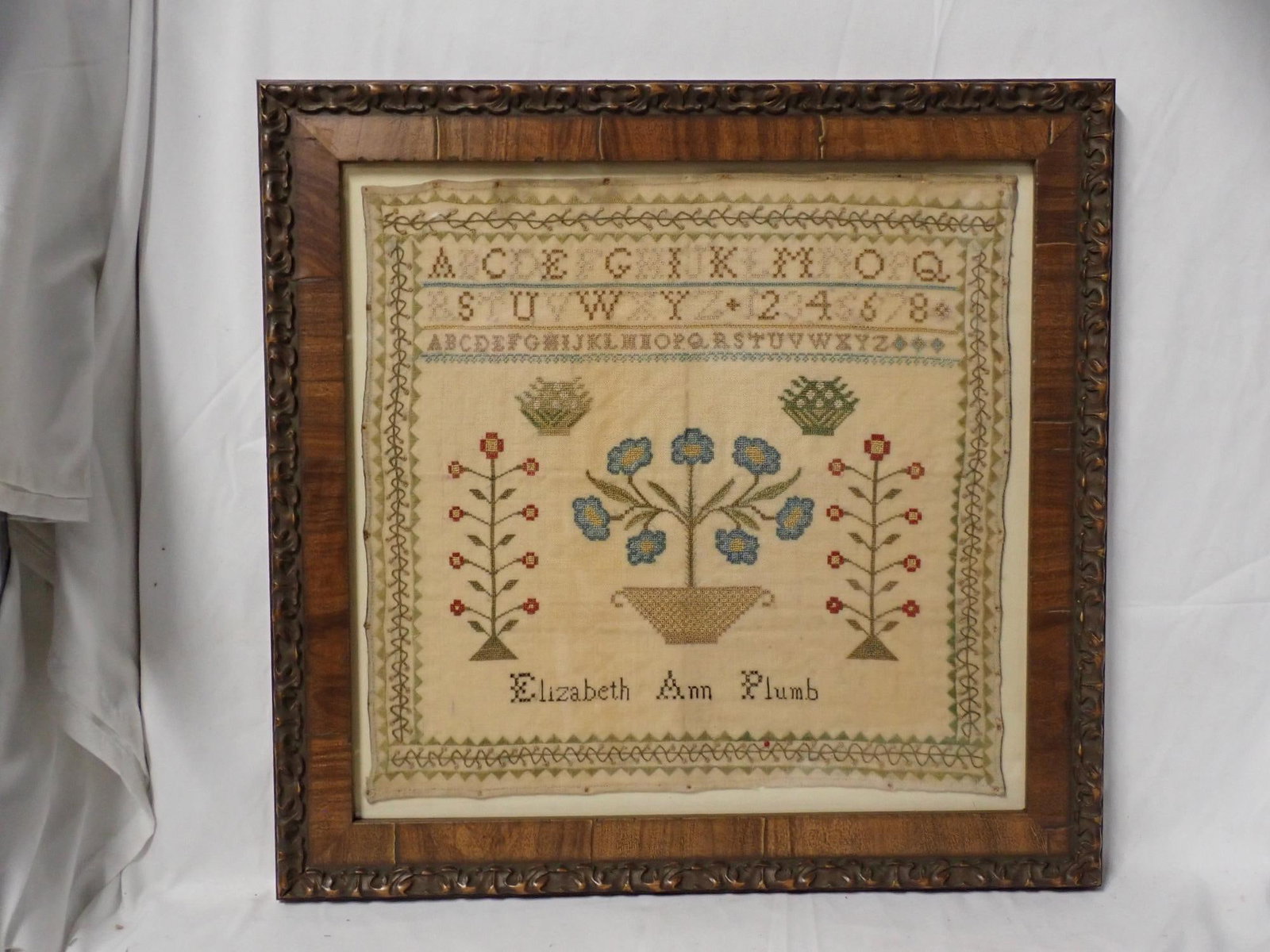Elizabeth Ann Plumb Sampler: Elizabeth Ann Plumb. Alphabet, Numbers, Motif is flowers and baskets. Vine and geometrical border. Some fabric discoloration. Frame 16 1/4" x 16 3/4" Sampler 12 1/2" x 13"