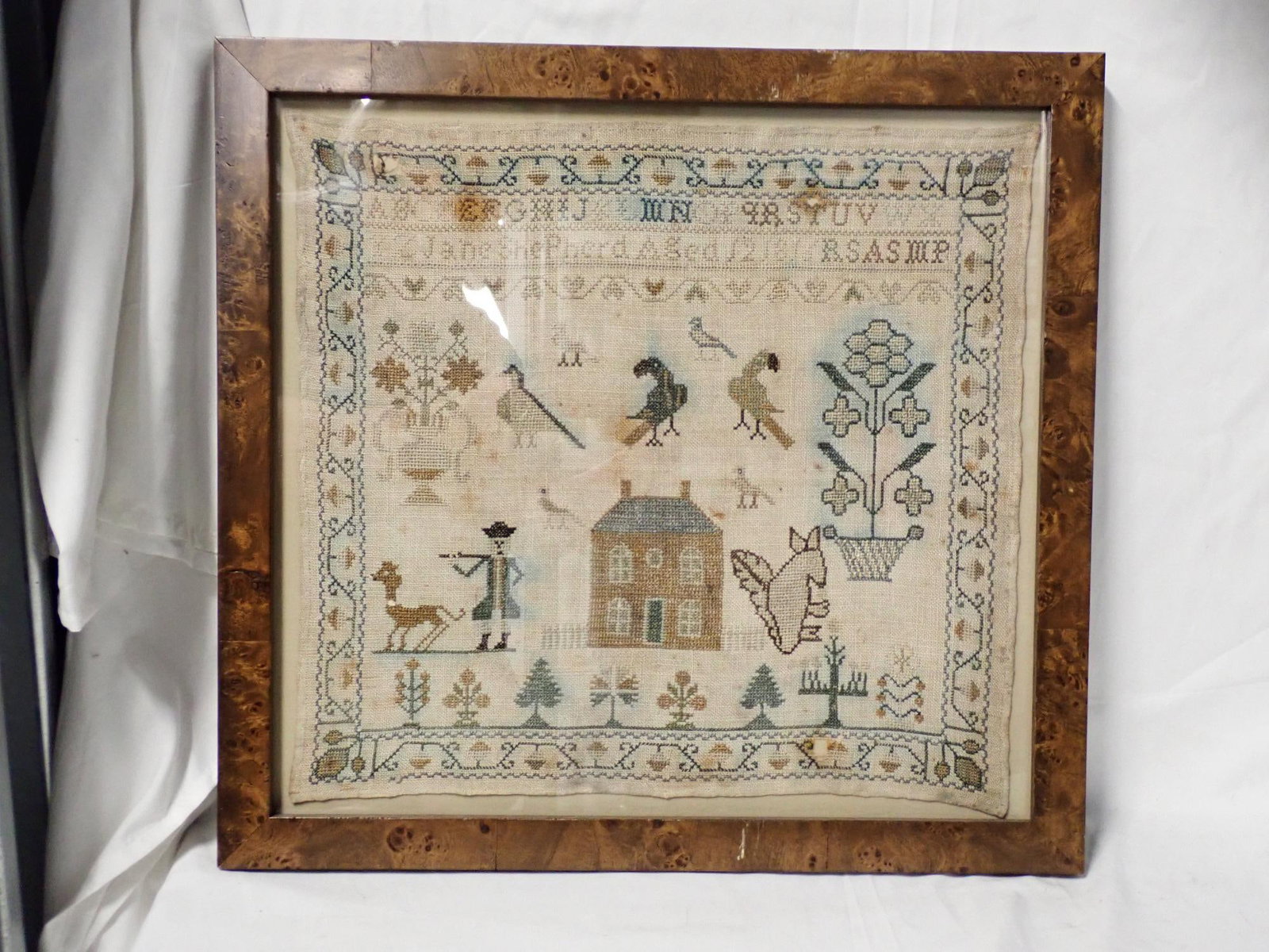 1816 Jane Shepherd Sampler: Jane Shepherd Aged 12 1816. Motif Man, House, birds, flowers, trees and urns. Vine and flower border. Some fabric loss staining and thread bleeding. Frame 17 1/4 x 18 1/4 Sampler 14 1/4 x 15 1/4
