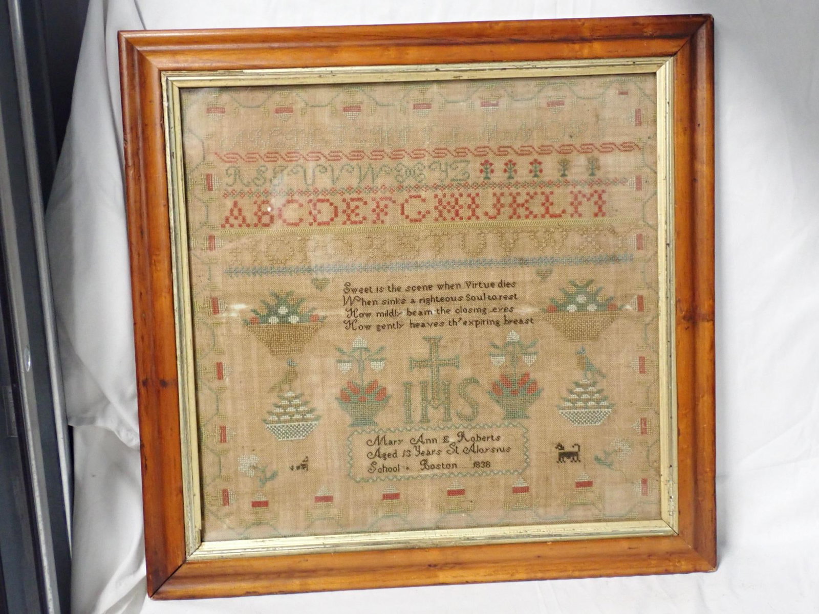 1838 Mary Ann E. Roberts Sampler: Mary Ann E Roberts Aged 13 Years St. St. Aloysius School Boston 1838. Verse in center with religious emblem Alphabet, baskets of flowers animals hearts Vine and geometrical flower border. Fabric