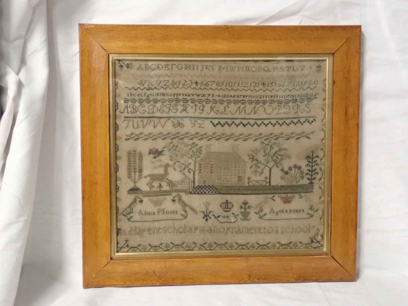 Mid 19th C Alicia Moses Sampler: Alicia Moses 184(?) Aged 8 years. A diligent scholar is an ornament to a school. Alphabet and numbers. Motif house stag, flowers baskets and trees. Vine and floral border. Fabric loss and staining