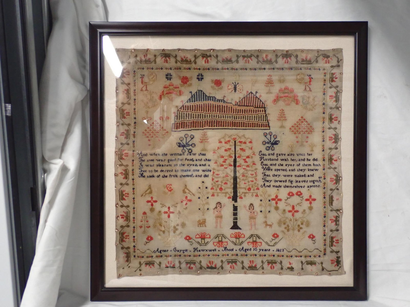 1853 Agnes Gaygill Sampler: Agnes Gaygill Hawxwell (?) School Aged 10 years 1853. Religious verse in center. Large building (?) above verse Adam and Eve center bottom Motif Flowers peacocks butterflies trees baskets of flowers.
