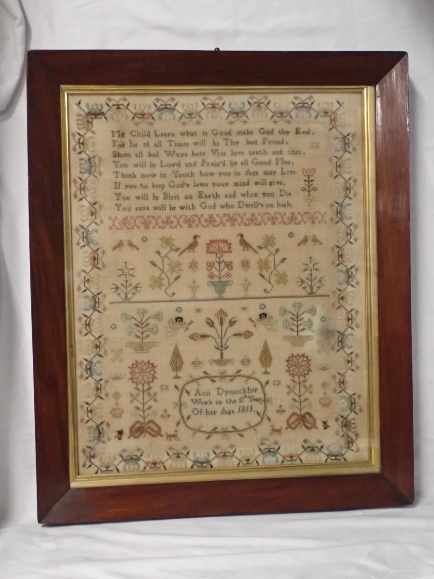 1811 Ann Dymock Sampler: Ann Dymock her Work in the 11th year of her age 1811. Religious verse at top. Motif cherubs, birds, flowers animals. Vine and floral border. Some staining and fabric discoloration. Frame 20 1/4 x 16