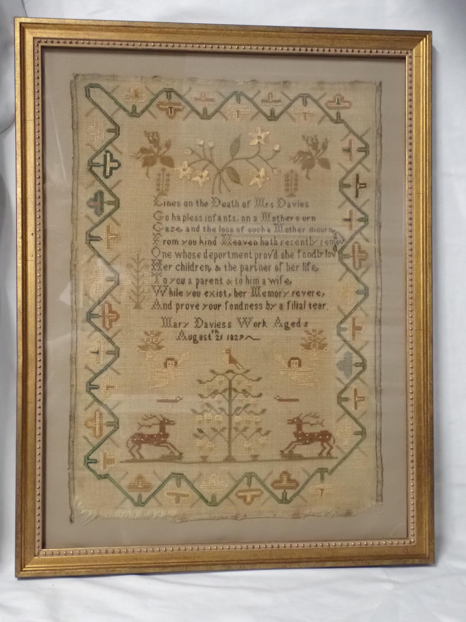 1829 Mary Davies Sampler: Mary Davies Work Aged (?) . Religious death verse in center. Motif cherubs stags, tress, flowers. Geometrical vine and floral borer. Fabric loss . Frame 22 1/2 x 17 1/4. Sampler 18 1/2 x 13