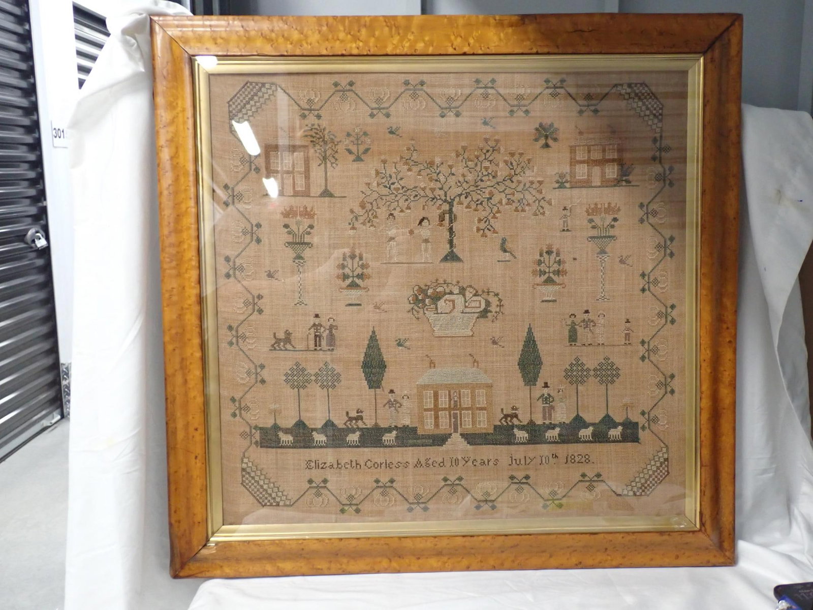 1828 Elizabeth Corless sampler: Elizabeth Corless aged 10 years July 10th 1828. Motif houses Adam and Eve trees, birds people flowers and animals. Vine floral and basket border. Fabric discoloration Frame 29 1/2 x 30 1/2 Sampler 23