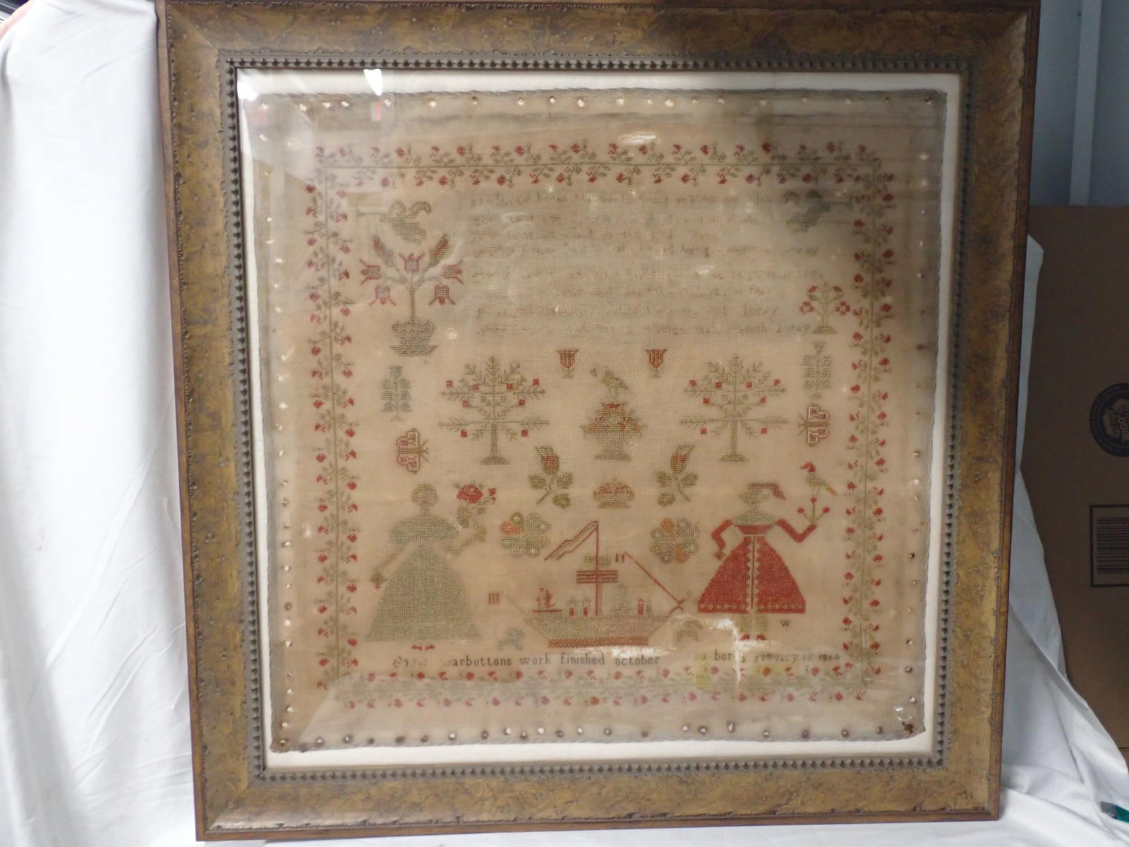 1826 Sarah Warbutton Sampler: Sarah Warbuttons work finished October illegible born January 15 1814. Religious verse (very illegible). Motif 2 Women ship trees flowers cherubs .Vine and floral border. Fabric loss thread loss and