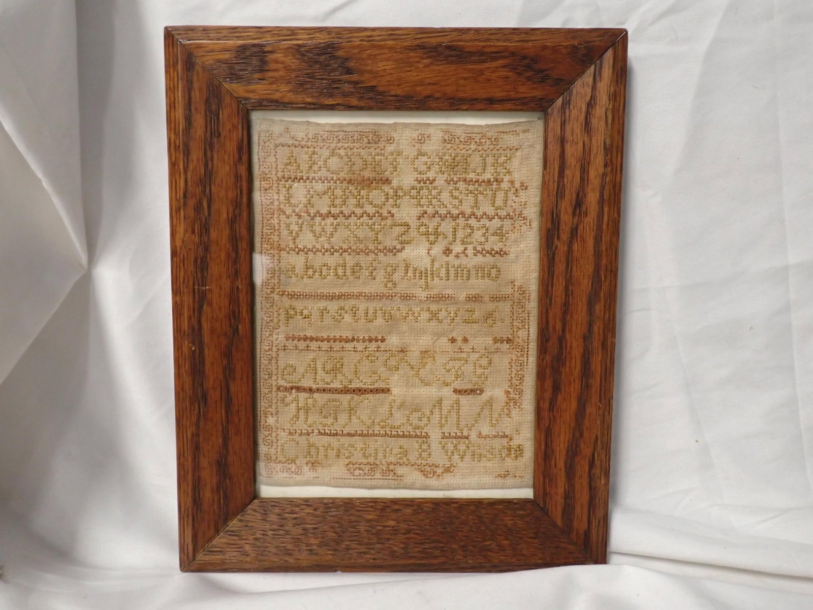 Christina Wilson (?) no date: Christina Wilson alphabet numbers geometrical border, Thread loss and staining. Geometrical border. Frame 10.3/4 x 8 3/4. Sampler 7.5 x 5.5