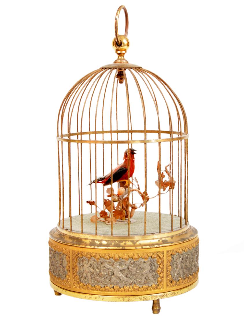 Gilt Bird Cage Feathered Mechanical Bird Wind Up: Vintage gilt ornate bird cage with a feathered bird perched on a branch. Wind it up and the little bird moves and chirps. 10"H. Condition report: Very good- wear on gilding. Please examine all photos 