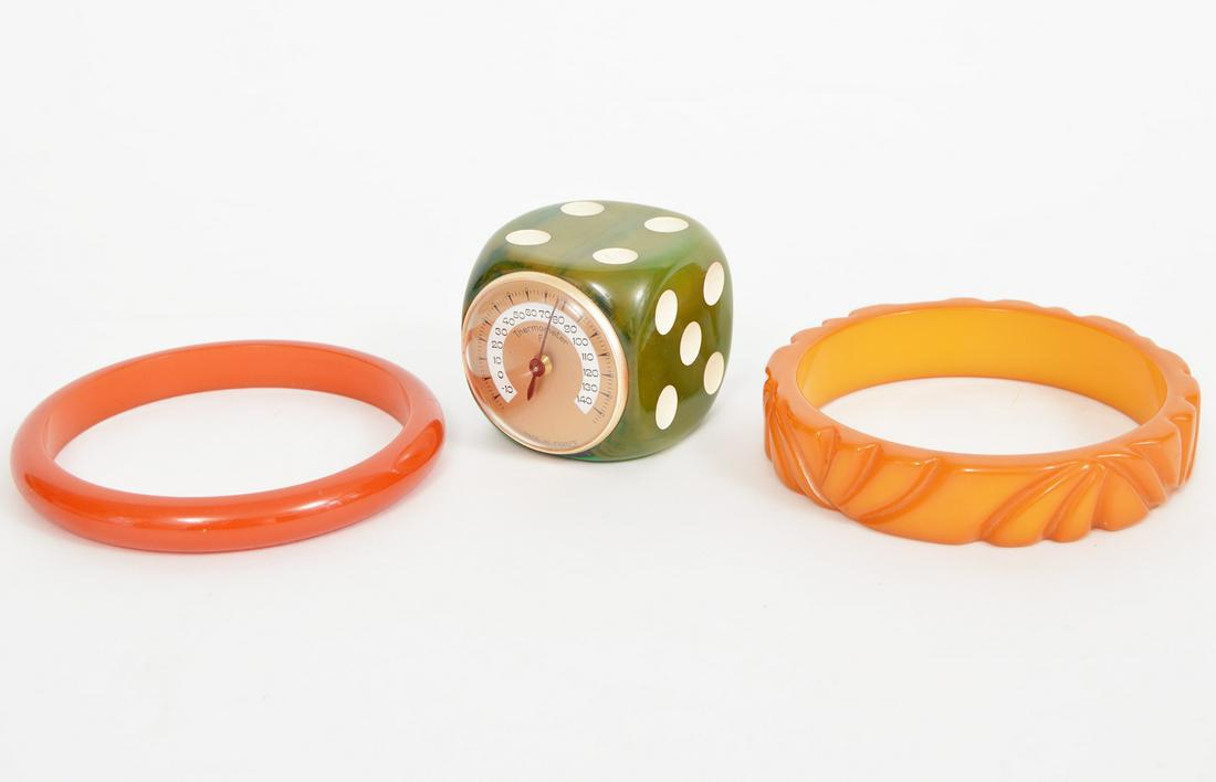 Bakelite Dice Thermometer & 2 Bangles: A lot of 3 Bakelite pieces: A dice with a working thermometer .5"x.5"x.5", a carved butterscotch bangle 5/8"wide, and an orange bangle 3/8" wide. Condition report: Very good - no issues. Please examin