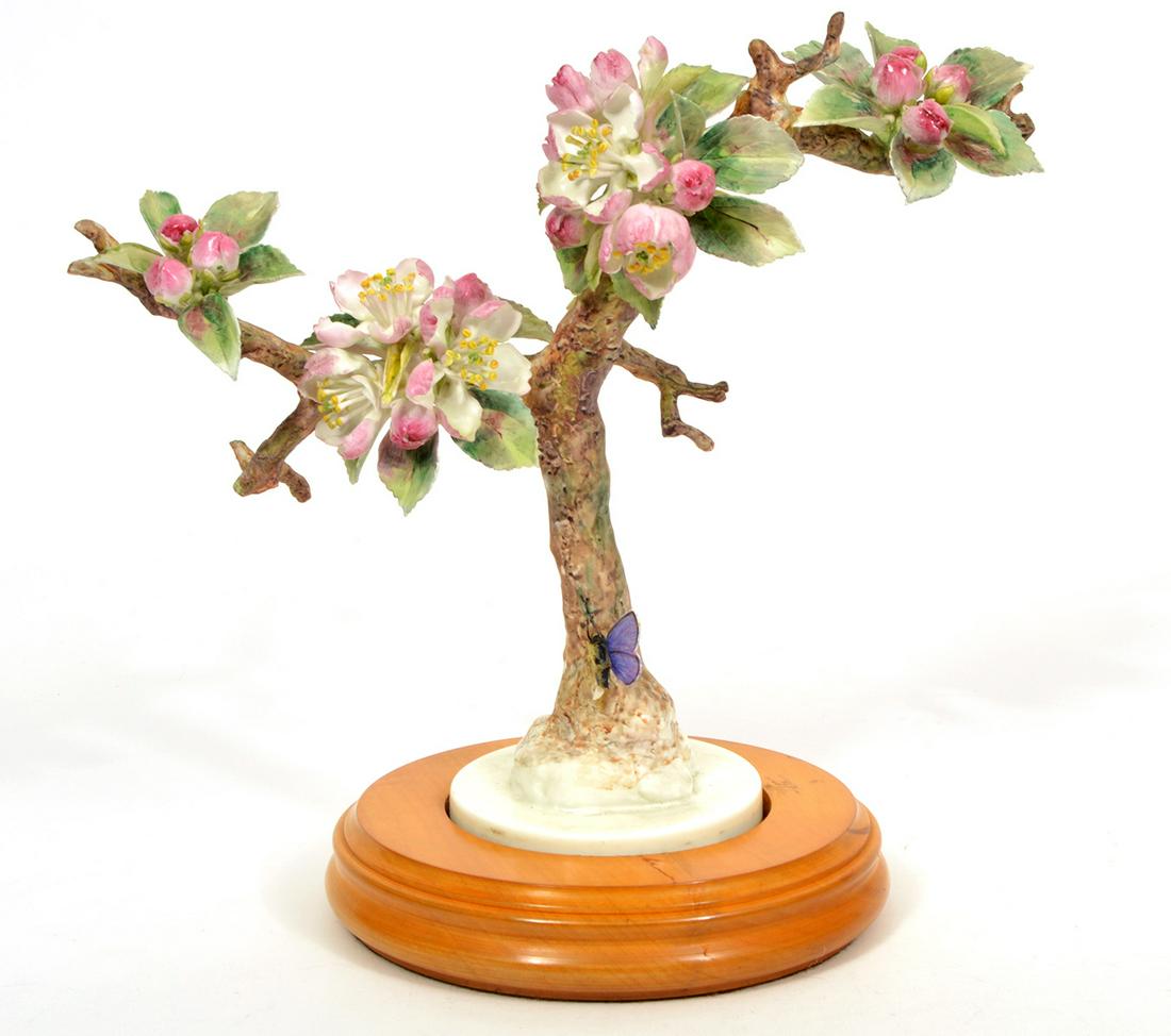 Royal Worcester Porcelain Flowering Branch: Royal Worcester porcelain figure of a flowering branch with a butterfly perched near the base. Attached to round wood base. Measures 10.5"H x 10.5"W x 6"D. Condition report: wing on butterfly is broke