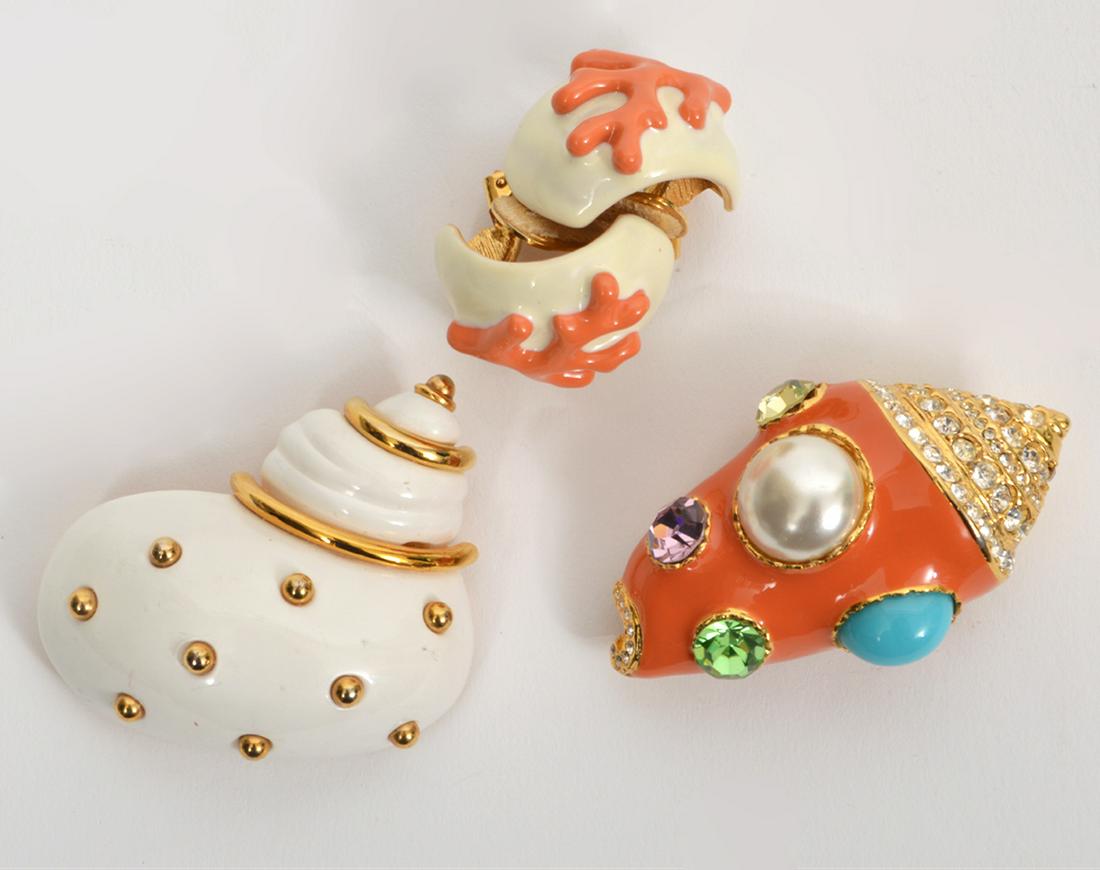 Kenneth Lane Earrings and 2 Brooches: Kenneth Lane clip on earrings feature gold tone backing with faux coral on white background (1" x 1"). White shell brooch with gold tone accents (2" x 1.75"). Peach shell shaped brooch with pearls and