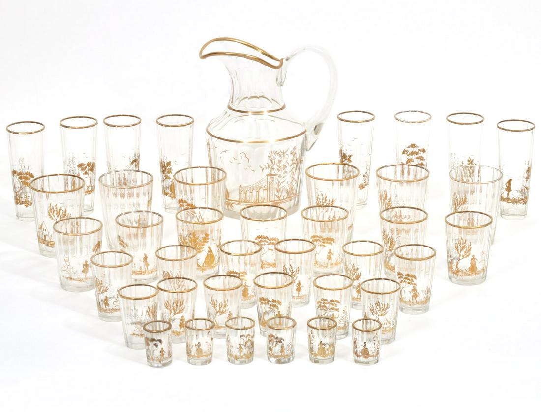 Style of Baccarat Pitcher and 39 Barware Glasses: Style of Baccarat ribbed pitcher with gilt trim and gilt landscape scene. Ribbed and gilt decorated matching glasses include 6 shot glasses 2"H; 6 tumblers @ 2 5/8"H; 6 cocktail glasses @ 3"H; 6 cockt