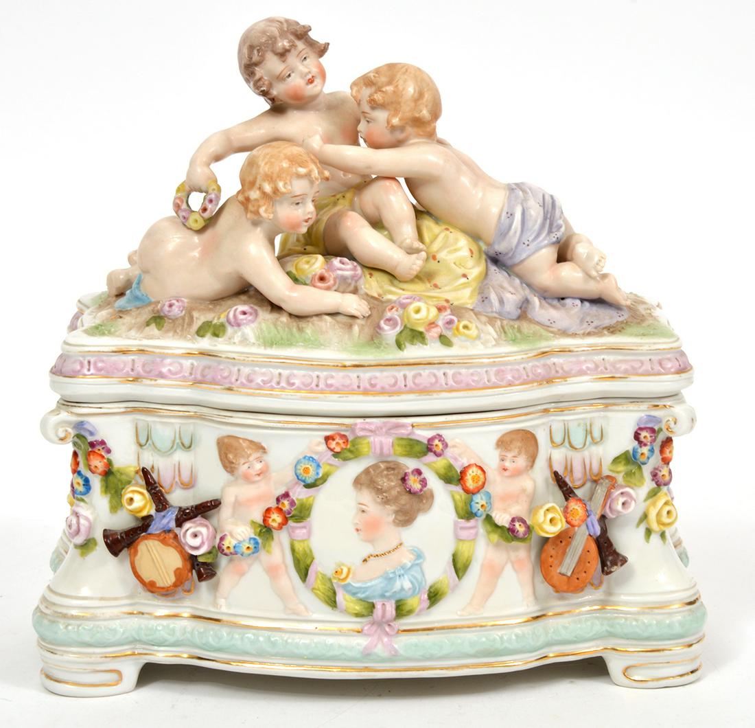 Meissen Style Decorative Lidded Porcelain Casket: Meissen style porcelain casket with 3 children on lid, accented overall with floral swags and gilt trim, raised on 4 small feet. Measures 8.5"L x 5"W x 8.5"H. Condition report: minor wear to surface p
